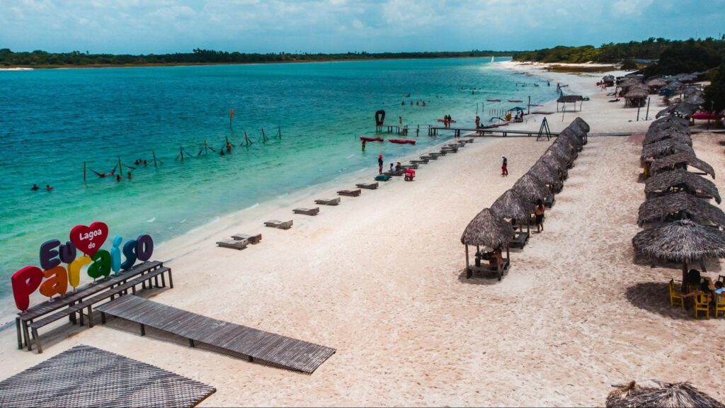 Orla da Praia de Jericoacoara com choupanas de praia e cadeiras dispostas ao longo da faixa de areia, em contraste com o mar esverdeado
