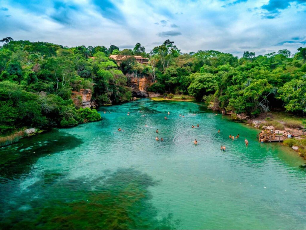 Banhistas em um lago do Parque Nacional da Chapada Diamantina, no interior da Bahia. A O lago está rodeado por uma vegetação densa e por formações rochosas alaranjadas.