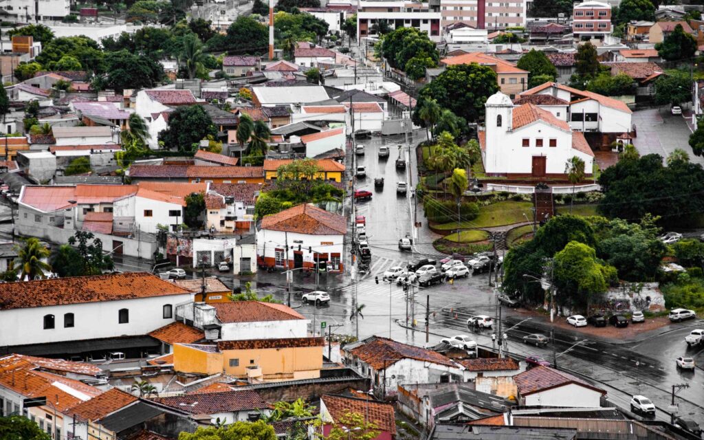 Visão aérea de parte da cidade de Cuiabá. As ruas estão molhadas e repletas de carros que cruzam as casas e prédios da cidade
