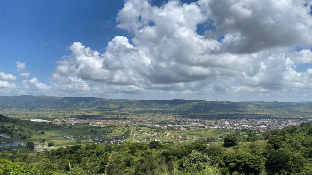 Vista aérea do município de Bonito, interior de Pernambuco. As construções da cidade aparecem distantes e formam um aglomerado em meio às montanhas verdes e aos trechos de mata.