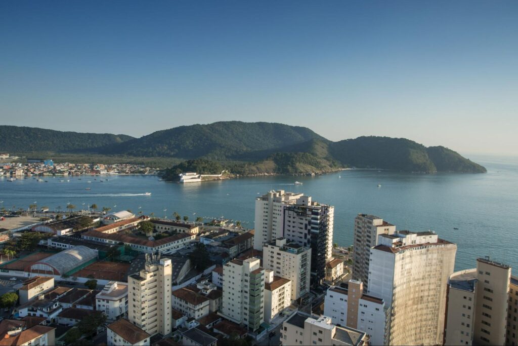 Vista aérea da cidade de Santos, com alguns prédios de diferentes tamanhos em frente a enseada.