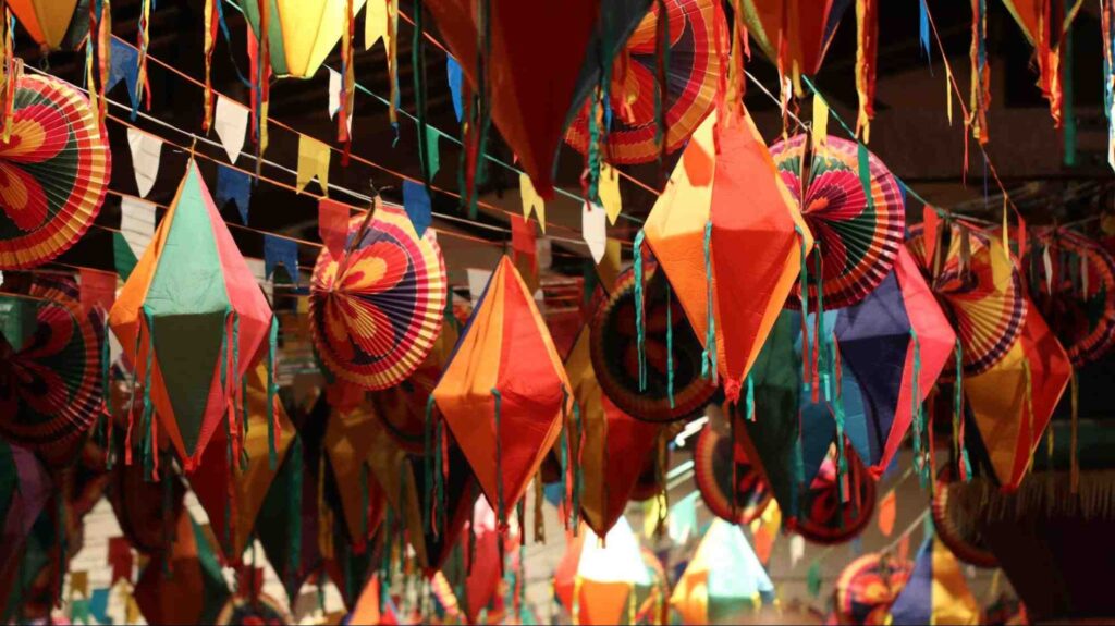 Balões e bandeirolas coloridas de papel, presas em cordões coloridas no teto, como parte da decoração de uma festa de São João.