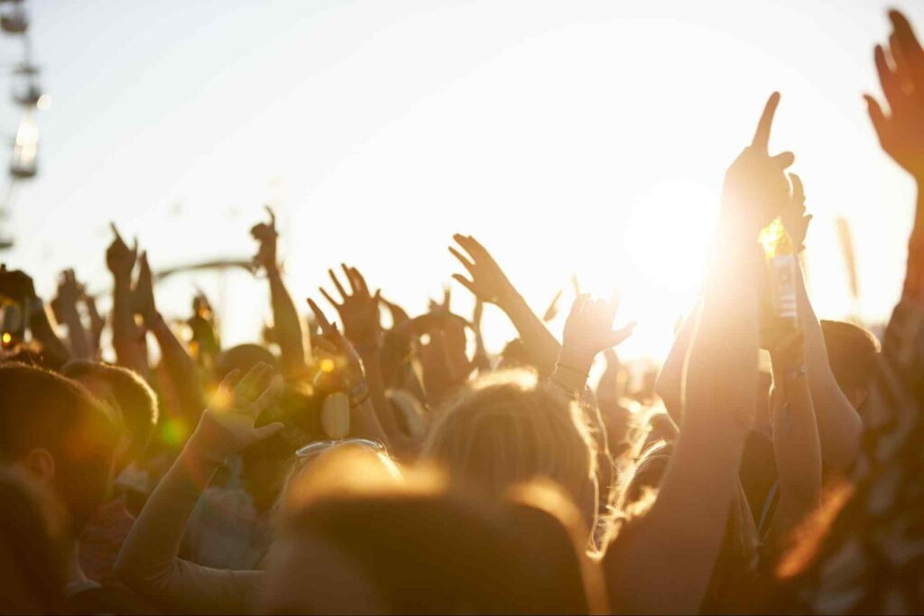 Público de festival de música a céu aberto com as mãos levantadas.