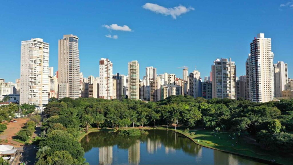 Foto panorâmica de Goiânia; na frente um lago, aos arredores árvores e prédios