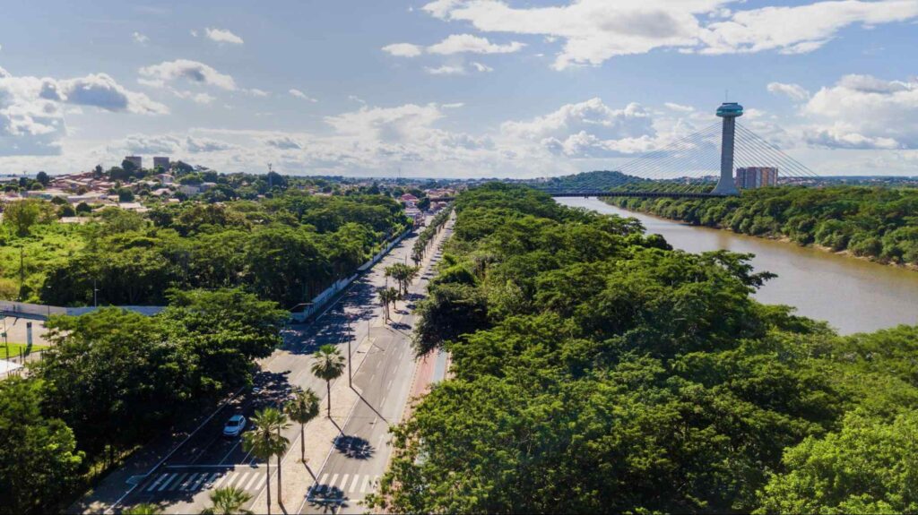 Foto aérea de Teresina, com uma rua no meio, arredores cercados por árvores e um rio no canto extremo direito.
