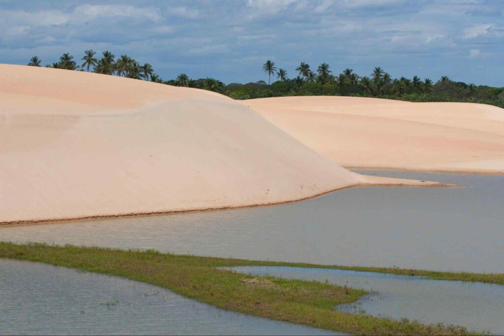 Águas calmas da Lagoa de Tatajuba, com dunas de areia branca e vegetação preservada ao fundo. O céu está azul e com poucas nuvens.