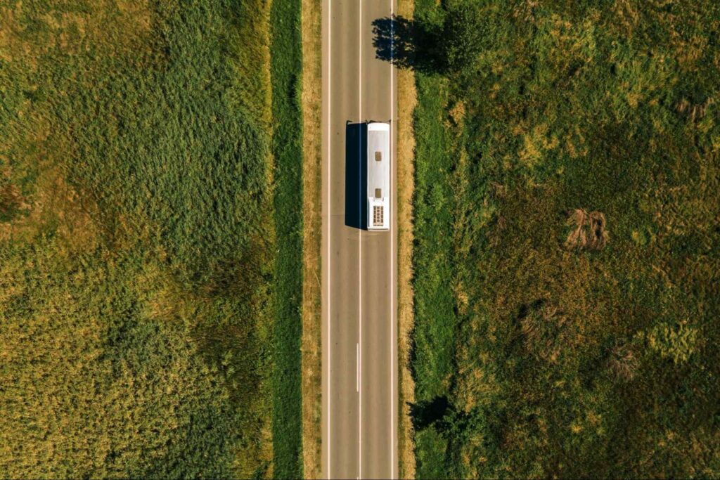 Vista aérea de ônibus na estrada, cercado por plantações verdes.