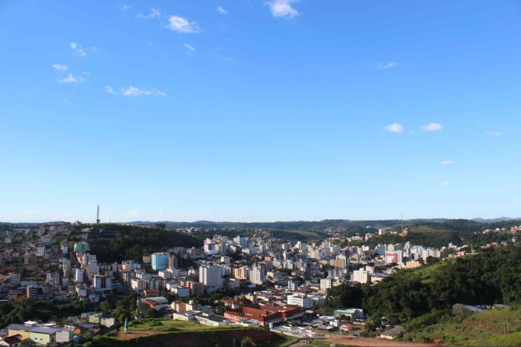 Vista aérea da cidade mineira Viçosa, com céu limpo e áreas verdes ao redor dos prédios.