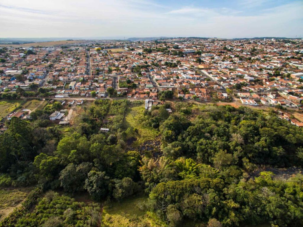 Vista aérea e panorâmica de parte da cidade de Botucatu, em contraste com a natureza que a cerca e céu parcialmente encoberto.