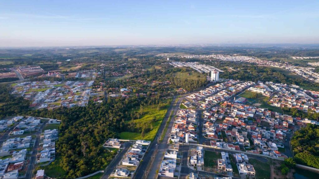 Paisagem aérea de parte da cidade de Indaiatuba SP, mostrando as casas em meio às árvores e bastante área verde. Céu limpo e azul.