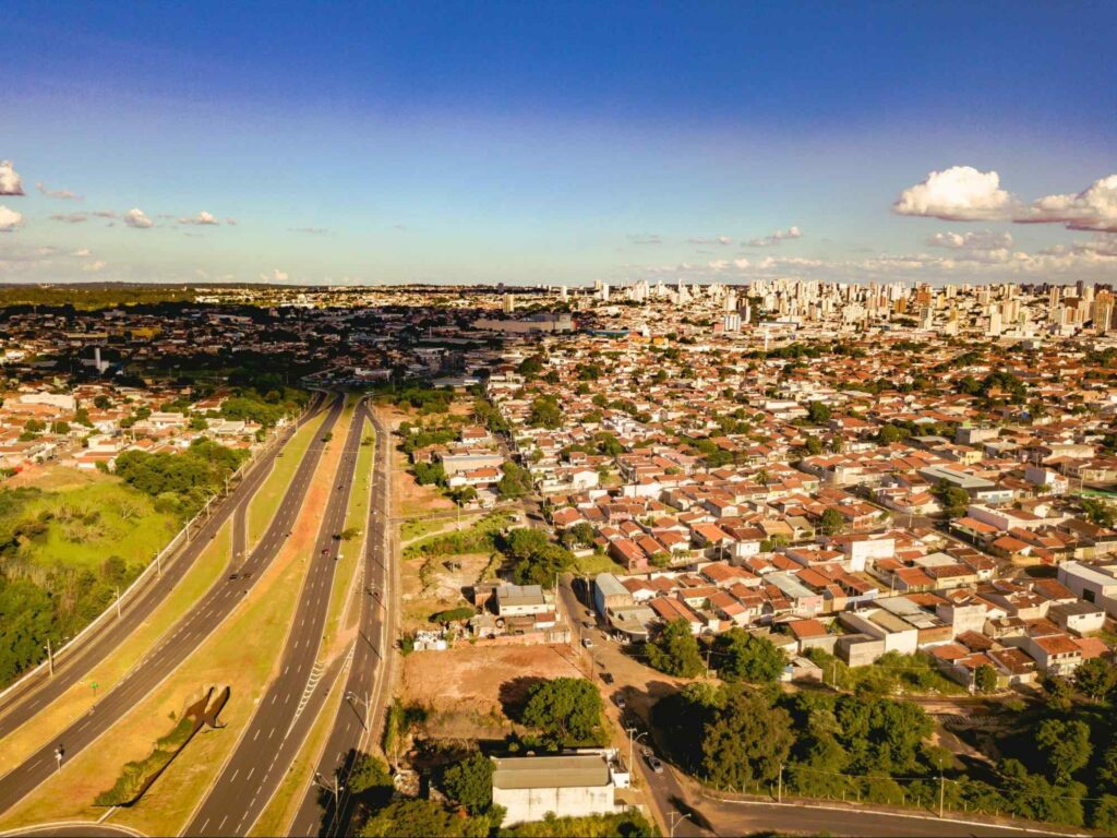 Paisagem aérea de parte da cidade de Bauru SP. Várias áreas verdes em meio à rodovia, casas e prédios.