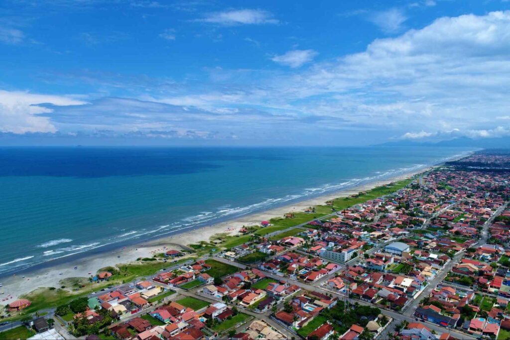 Vista aérea de parte da cidade de Itanhaém, mostrando o azul do mar combinando com o azul do céu e o contraste com as casas em frente à praia.