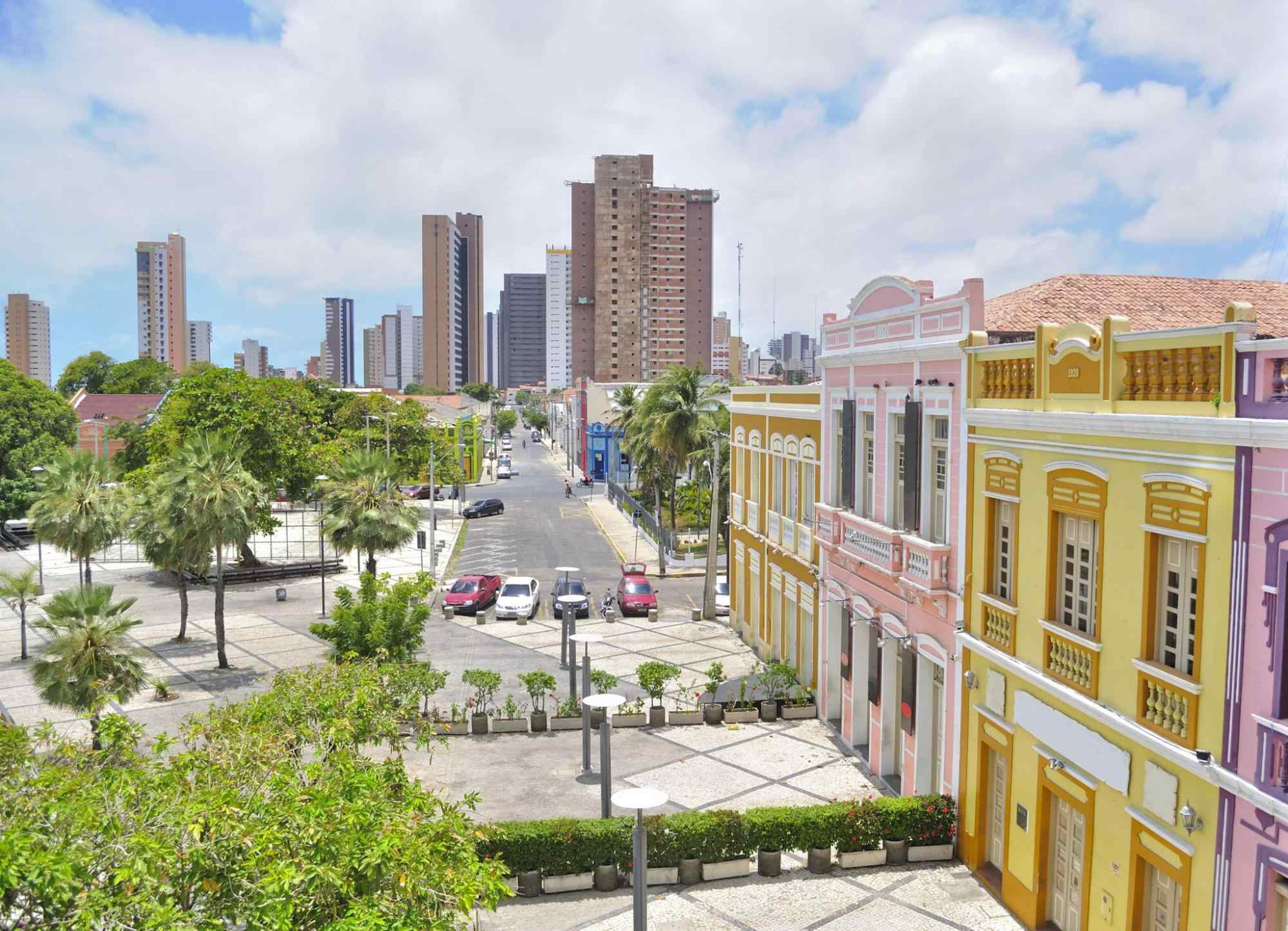 Vista aérea mostrando parte lateral do centro de Fortaleza, com as casas coloridas que formam o Centro Cultural Dragão do Mar. Prédios e alguns carros aparecem ao fundo.