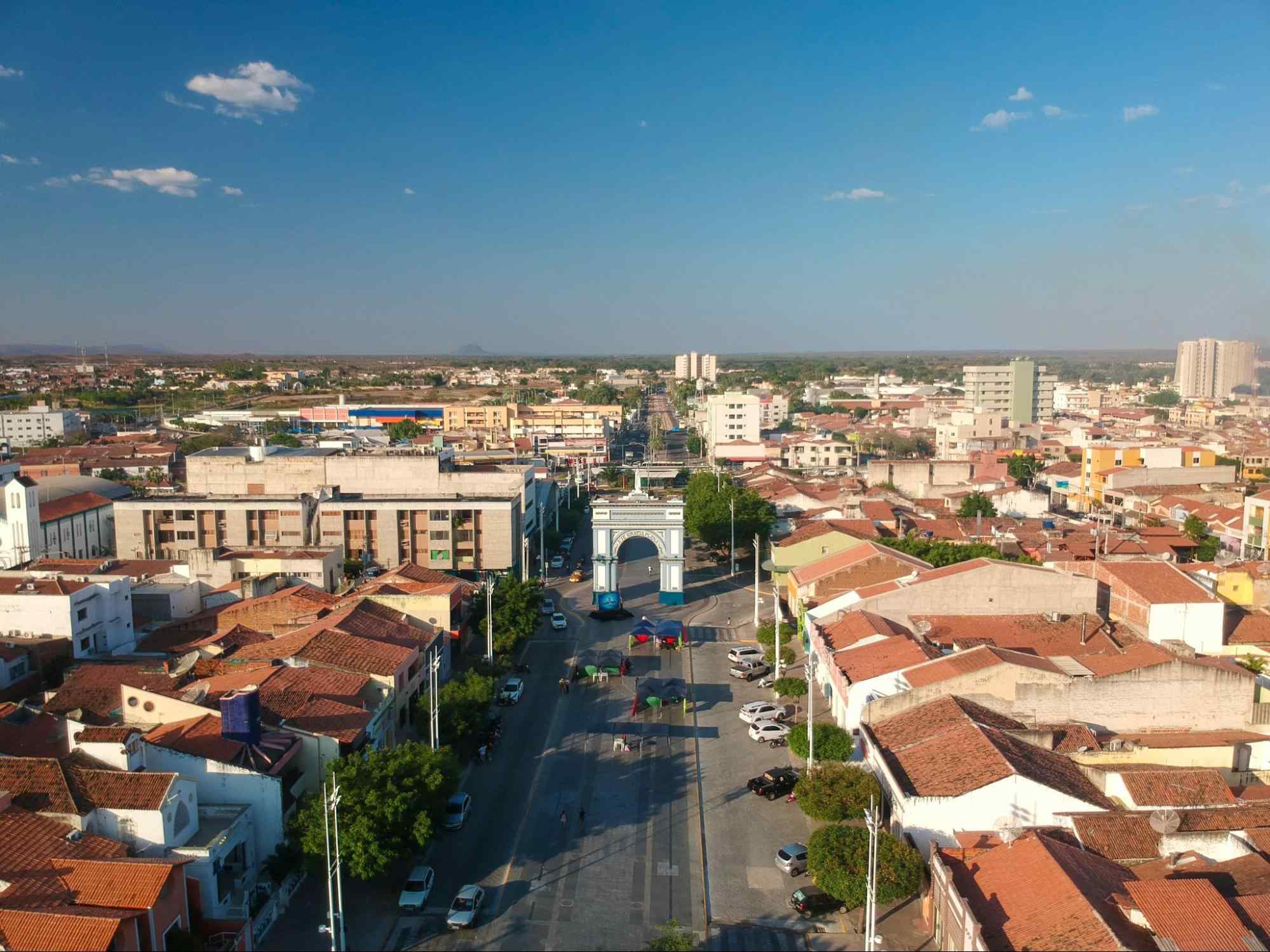 Imagem aérea de Sobral, Ceará. No centro da foto está uma grande avenida que atravessa um monumento azul e branco em forma de arco. Dos dois lados da via, há muitas construções baixas.
