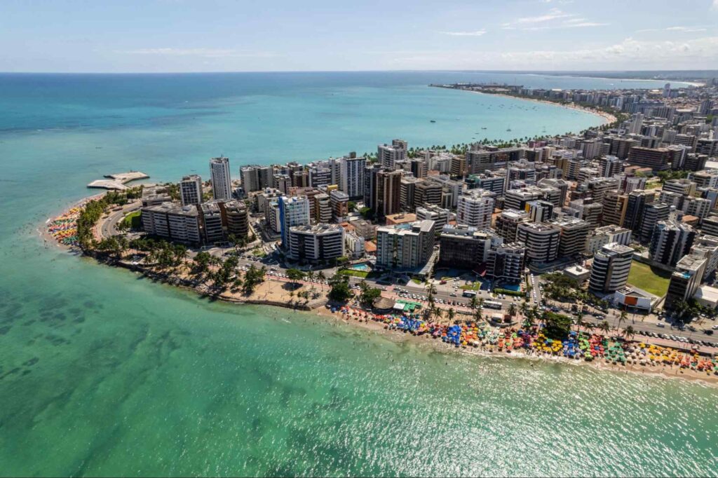 Vista panorâmica da cidade de Maceió, com a orla da praia, aguás esverdeadas e os prédios da cidade