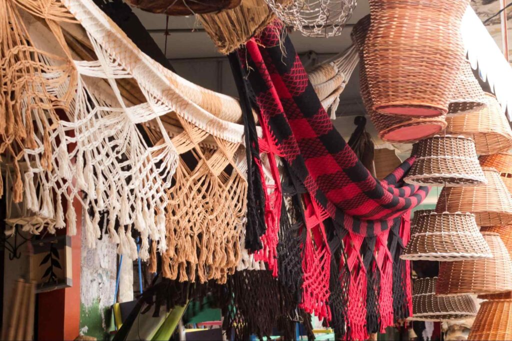 Redes de tecido e cestos de palha expostos para venda em mercado público de Recife.