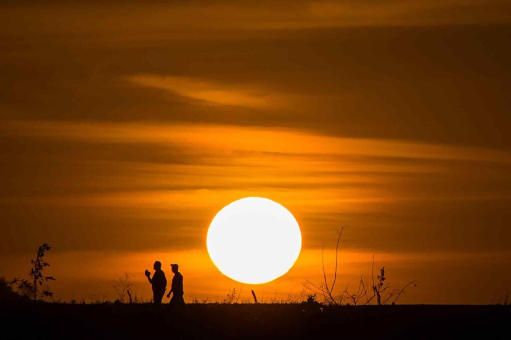 Pôr do sol no interior de Pernambuco, com as silhuetas de duas pessoas que caminham no horizonte