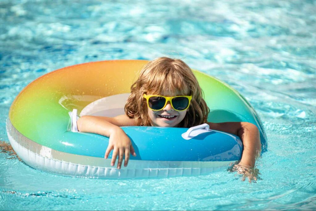 criança na piscinas usando uma bóia colorida e óculos escuros, sorrindo