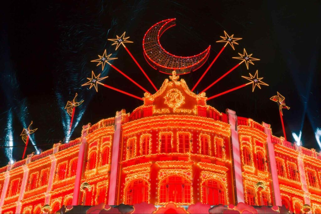 Parte da fachada do Palácio Avenida, em Curitiba, durante o Natal. O palacete está inteiramente coberto por pequenas luzes douradas e vermelhas. No topo, há arranjos luminosos com formatos de lua e estrelas