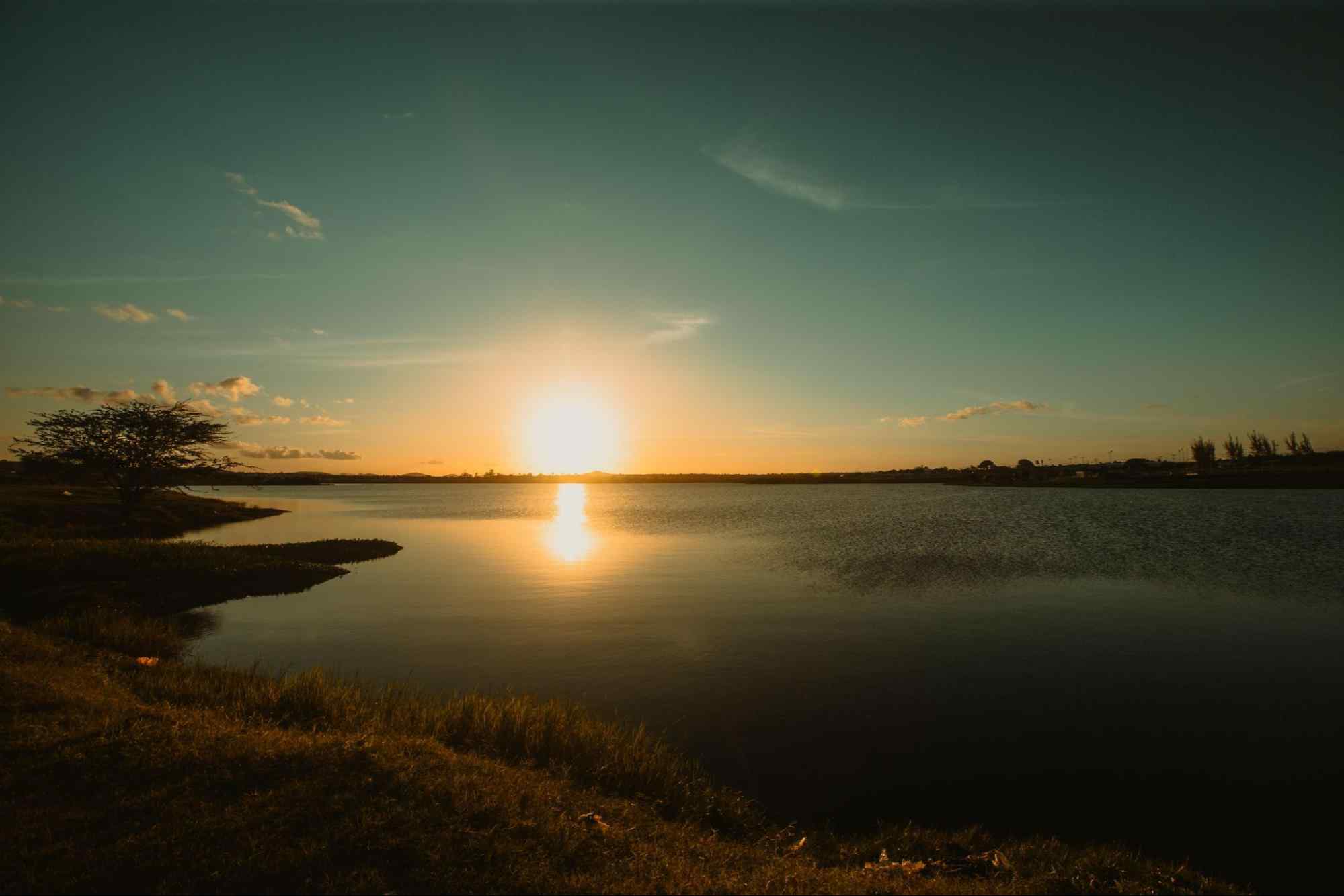 Pôr do sol no Lago Perucaba. Luz amarela refletindo nas águas calmas, com céu quase sem nuvens