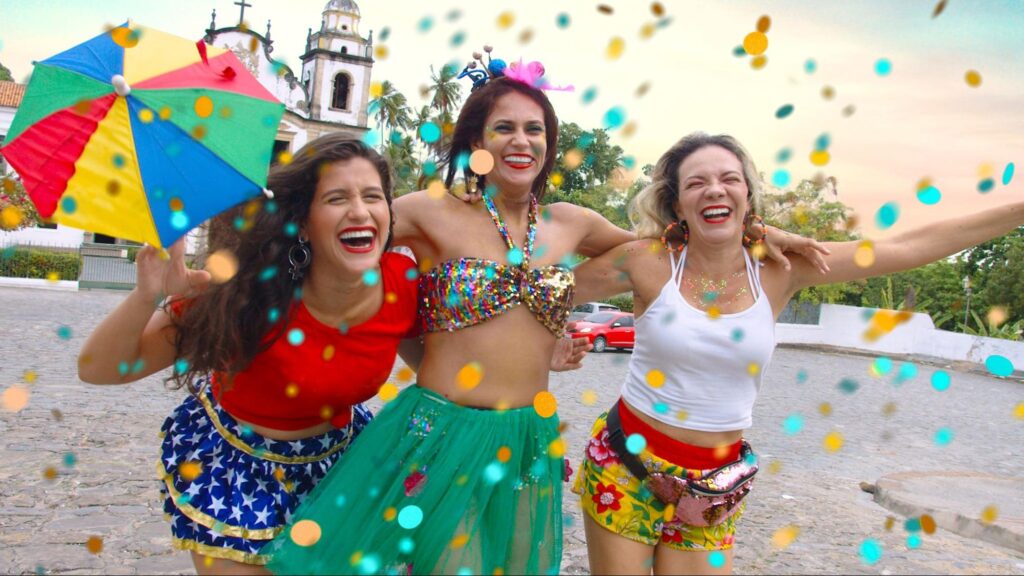 Jovens sorridentes reunidos em uma festa ao ar livre. Eles usam acessórios carnavalescos coloridos