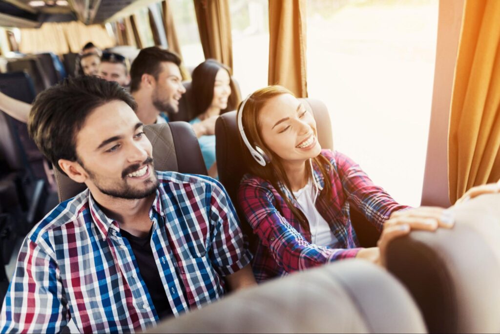 Pessoas dentro de um ônibus de turismo sorrindo enquanto olham pela janela