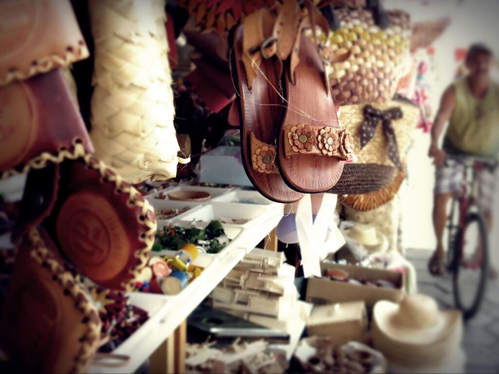 Artigos expostos para venda em um quiosque da Feira de Caruaru. A seleção de produtos artesanais inclui calçados de couro, chapéus de palha, brinquedos de madeira, bolsas de materiais diversos e outros