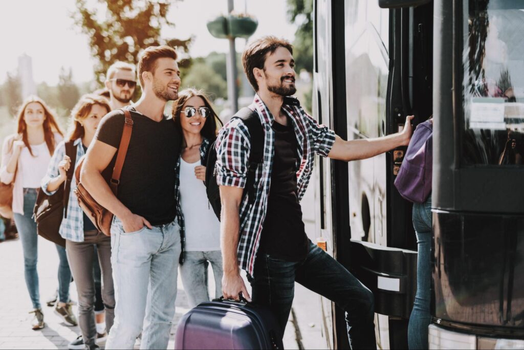 Homem entrando em um ônibus com uma mala de mão e uma fila de outras pessoas aguardando o embarque