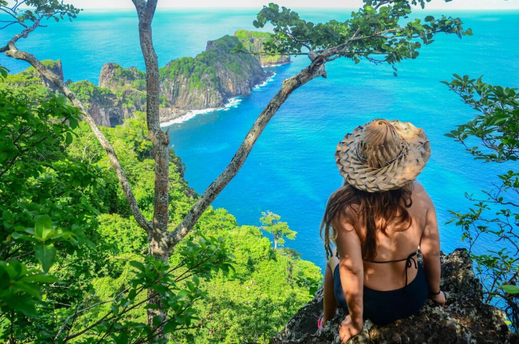 Mulher sentada em um mirante com a praia de Fernando de Noronha ao fundo